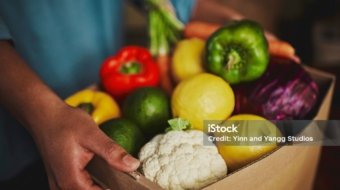 An unidentifiable person holding a box of fresh fruit and vegetables