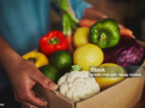 An unidentifiable person holding a box of fresh fruit and vegetables